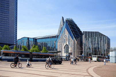 Modern glass building of Leipzig University in Augustusplatz, Germany, with people walking and cycling in the foreground on a sunny day.