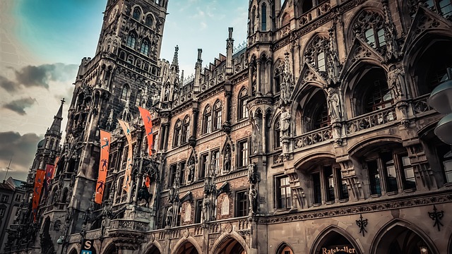Gothic-style facade of the New Town Hall (Neues Rathaus) in Munich, with ornate arches, statues, and red decorative banners hanging from the building.